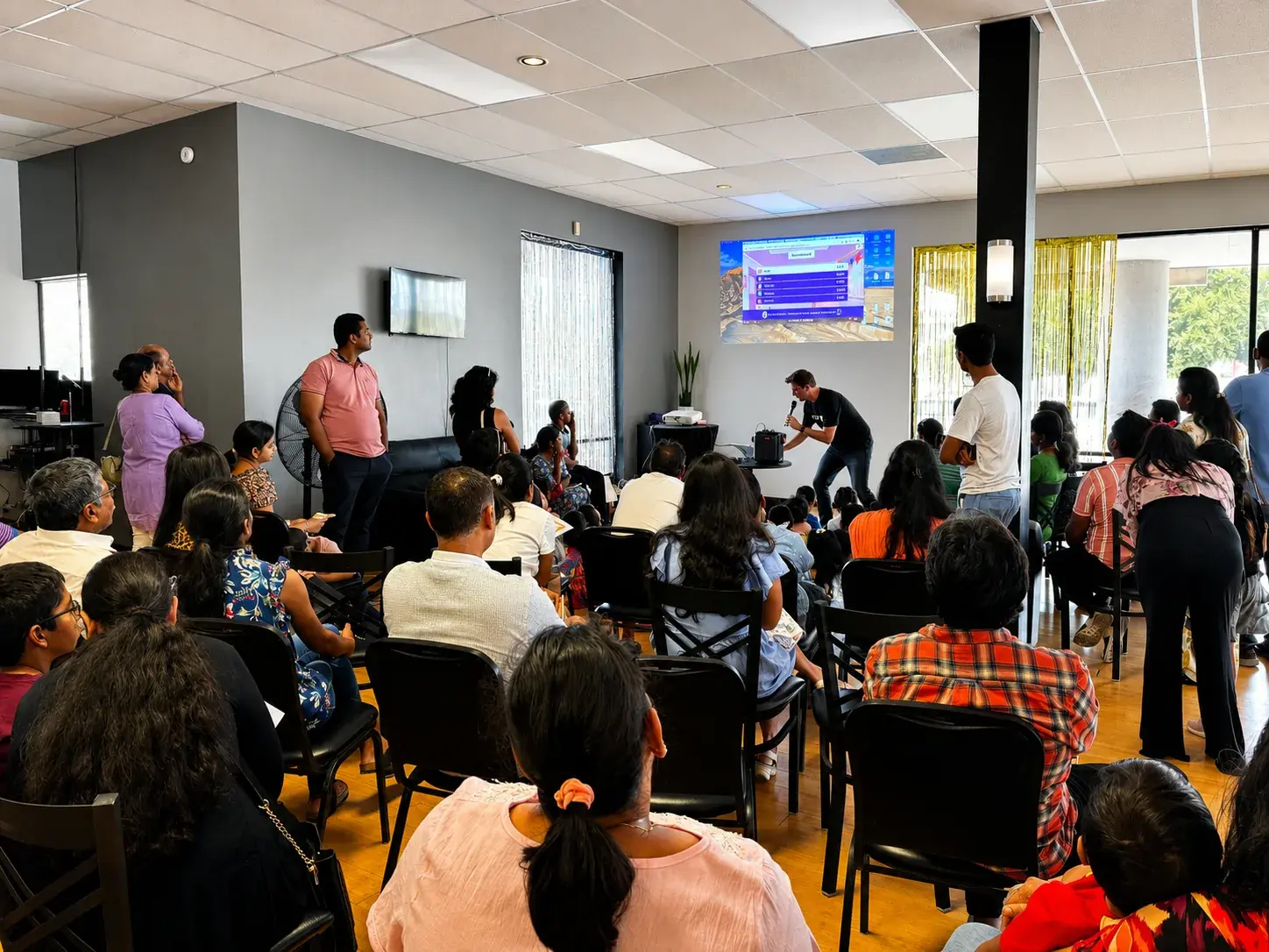 Parents and children seated in a packed room at a Cuemath math event, watching a live math quiz on screen