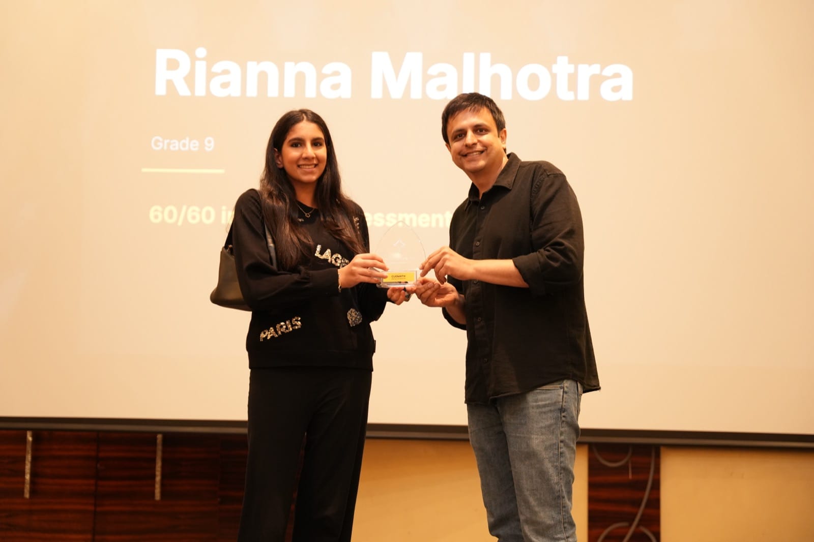A student receiving her award on stage from Manan Khurma at the Cuemath Parent Summit